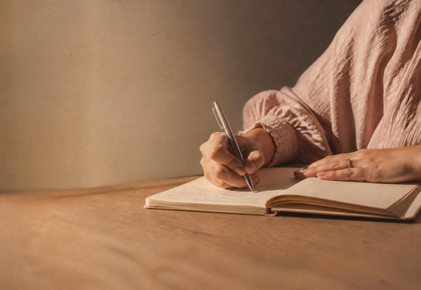 Mãos escrevendo à caneta em um caderno de papel sobre mesa de madeira
